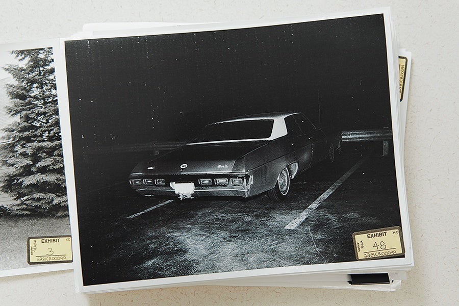 Black and white photo of a vintage car parked in a dark parking lot, viewed from the rear. The car is positioned between two white parking lines, and the photo has an "EXHIBIT 48" label in the bottom right corner.