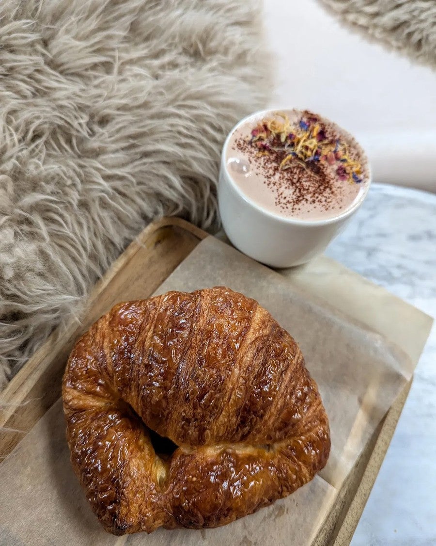 A croissant and hot chocolate sit on a marble table next to faux fur upholstery.